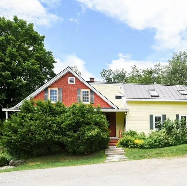 Farmhouse exterior behind overgrown shrubs